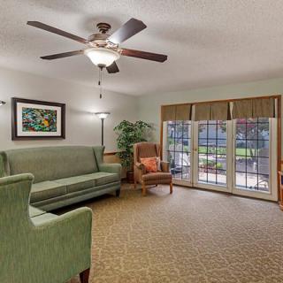 A cozy living room featuring a ceiling fan, sofa, armchair, and large glass doors leading outside.