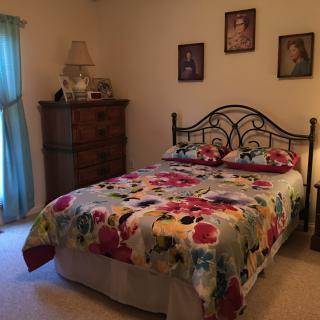 A cozy bedroom with a floral bedspread and decorative portraits on the wall.
