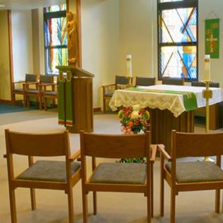 A small chapel interior with an altar, chairs, and stained glass windows.