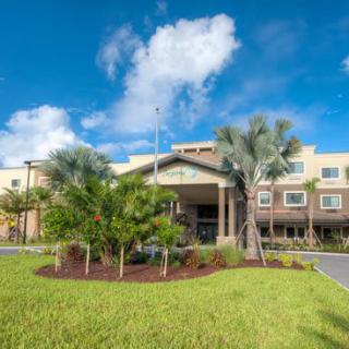 A hotel building with palm trees and a well-maintained lawn under a bright blue sky.