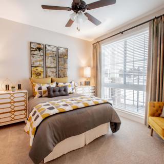 A modern bedroom featuring stylish decor with a comfortable bed, decorative pillows, and ample natural light streaming through large windows.