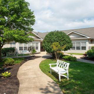 A peaceful garden with a bench and a winding pathway leading to a building.