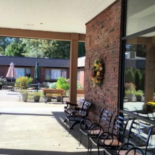 A cozy outdoor patio with chairs and a wreath on the brick wall, overlooking a courtyard.