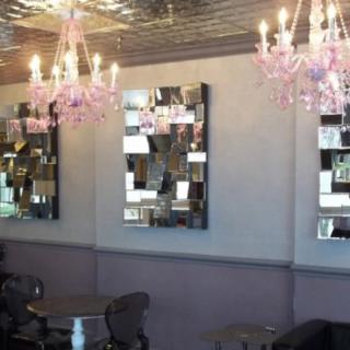 A stylish cafe interior featuring pink chandeliers and modern mirrors.