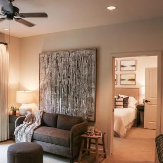A cozy living room with a sofa, artwork on the wall, and a glimpse into a bedroom.