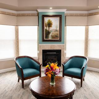 A cozy living room with two teal chairs, a fireplace, and a round table with a vase of flowers.
