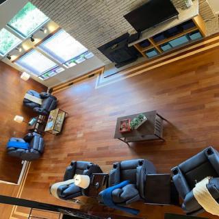 A spacious living room with hardwood floors, featuring multiple sofas, a central coffee table, and a television setup near large windows.