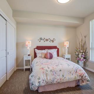 A cozy bedroom featuring a bed with floral bedding, flanked by nightstands and lamps, with decorative elements throughout.