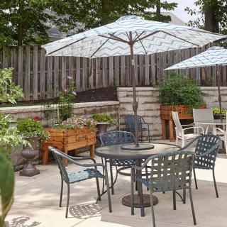 A cozy patio area with a table and chairs set under large umbrellas, surrounded by lush greenery and potted plants.