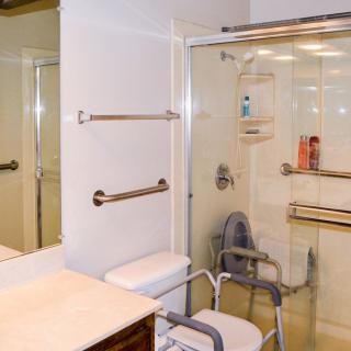 An accessible bathroom featuring a shower with handrails and a shower chair.