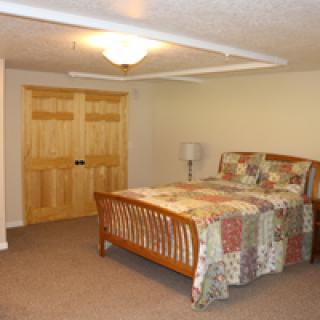 A cozy bedroom with a wooden bed and quilt, featuring carpeted flooring and wooden closet doors.