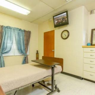 A hospital room with a bed, wall-mounted TV, window curtains, and a clock.
