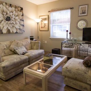 A cozy living room featuring a floral-patterned sofa and matching ottoman, a glass-top coffee table, and elegant wall art.