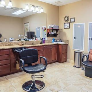 A clean and well-organized salon interior featuring a styling chair, mirrors, and cabinets.