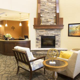 The image shows a cozy lobby area with a stone fireplace, comfortable seating, and a reception desk in the background.