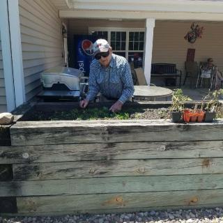 A person tends to plants in a raised garden bed outside a house.