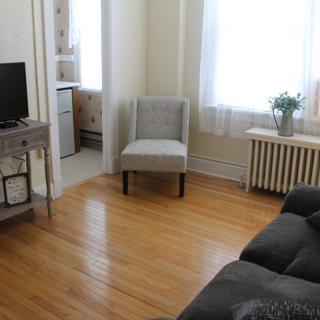 A cozy living room with a sofa, chair, television, and natural light from a large window.