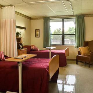 A hospital room with two beds and a chair by the window.