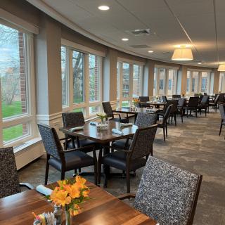 A modern dining area with neatly arranged tables and chairs, featuring large windows and decorative flowers.