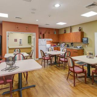 A cozy kitchen and dining area with multiple tables and chairs, featuring wooden cabinets and a refrigerator.