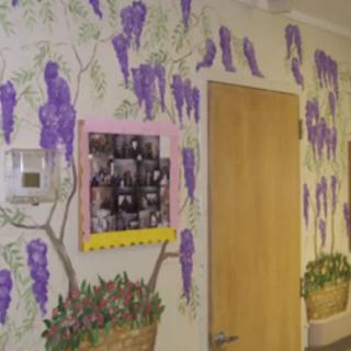 A hallway with a vibrant wall mural featuring purple flowers, a wooden door, and a photo collage.
