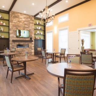A cozy dining area featuring round tables, comfortable chairs, a stone fireplace, and elegant chandelier lighting.