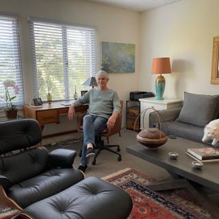 A man sits comfortably in a well-furnished living room with ample natural light.