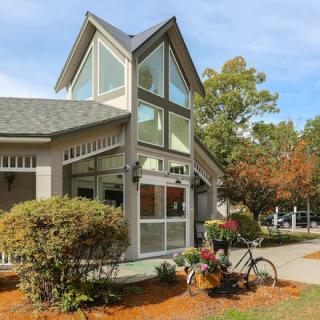 A modern building with a prominent glass facade and an outdoor bicycle stand, surrounded by greenery on a sunny day.
