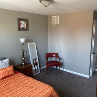 A minimalist bedroom with orange bedding, a standing lamp, a decorative mirror, and a red chair.