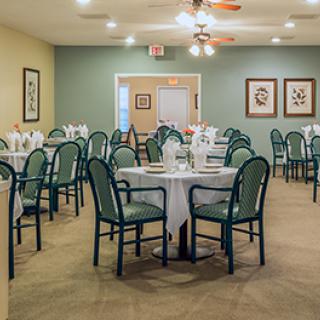 A neatly arranged dining room with round tables and green chairs, set for a meal.