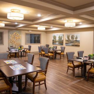 A well-lit dining area with neatly arranged tables and chairs, featuring elegant decor and artwork.