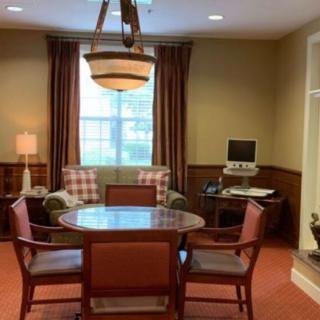 A cozy meeting room featuring a round table surrounded by chairs, a lamp, and a computer in the corner.