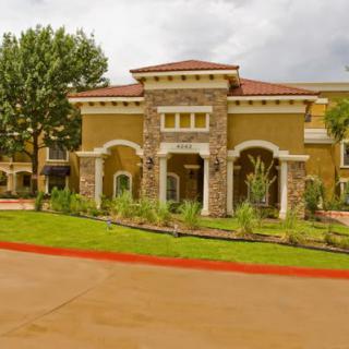 A modern building with an elegant stone entrance, surrounded by greenery and a cloudy sky.