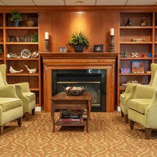 A cozy living room with green armchairs and a fireplace surrounded by bookshelves.