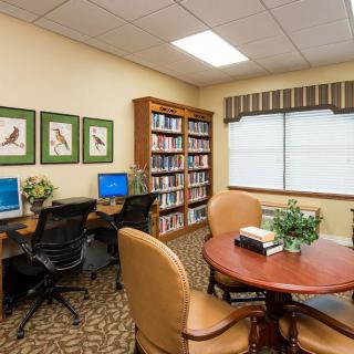 A small library room with computers, bookshelves, and a round table with chairs.