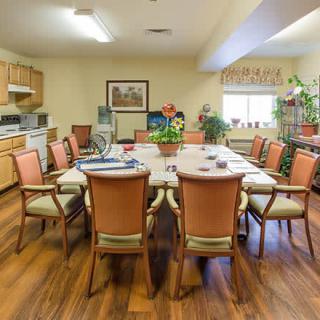 A well-furnished conference room with a large meeting table surrounded by chairs and featuring a small kitchen area.