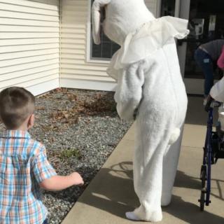A child follows a person in a bunny costume along a sidewalk.