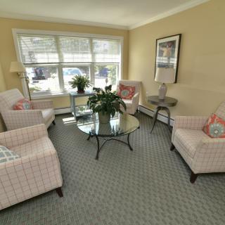 A cozy living room featuring comfortable chairs, a glass coffee table, and large windows allowing natural light.