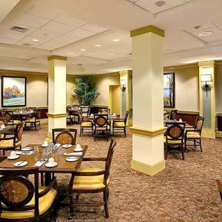 An elegant dining area with neatly arranged tables and chairs, carpeted flooring, and decorative artwork on the walls.