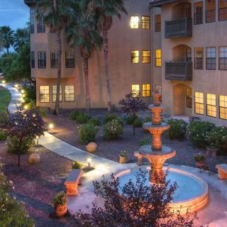 A beautifully illuminated courtyard with a central fountain, surrounded by apartment buildings and lush greenery in the evening.