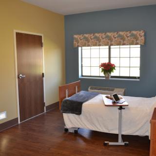 A well-lit hospital room featuring a single bed, a window with curtains, and minimal furniture.