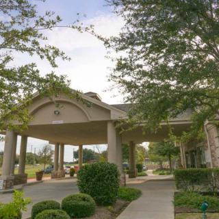 A well-landscaped building entrance featuring trees and bushes along a pathway.