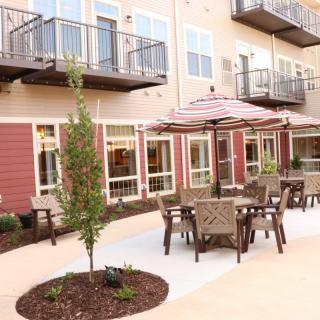 Outdoor patio area with tables, chairs, and umbrellas in front of an apartment building.