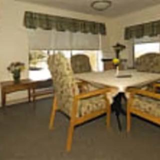 A cozy dining room with a table and four chairs, adorned with floral patterns, set by large windows with green curtains.