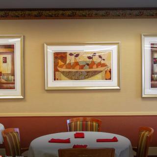 A restaurant interior featuring framed paintings on the wall and a dining table with chairs.