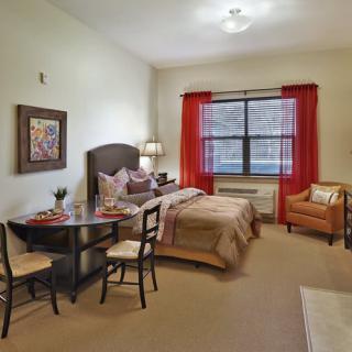 A modern bedroom interior with a bed, table, chairs, and a window with red curtains.