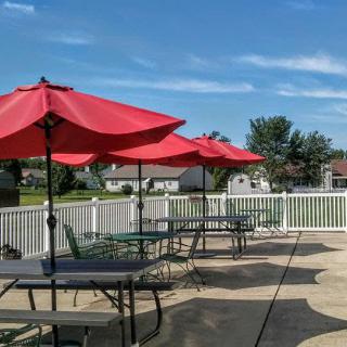 A sunny outdoor patio with red umbrellas shading tables and chairs.