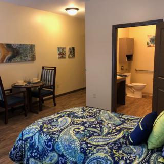 A cozy bedroom with a vibrant bedspread, an adjoining bathroom, and a small dining area.