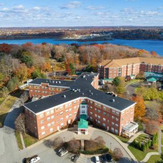 Aerial view of a campus with brick buildings surrounded by autumn trees and a lake in the background.