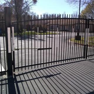A black metal gate casting shadows on the pavement in a well-lit outdoor area.